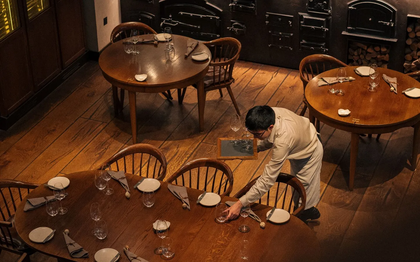 Restauranglokal i varmt ljus där personal dukar borden